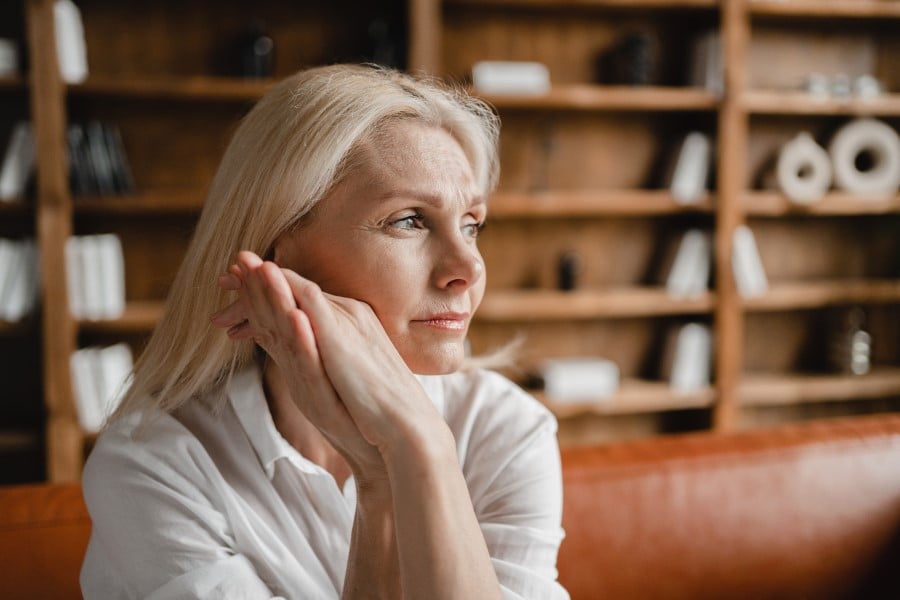 Osoba na zdjęciu wygląda na zamyśloną, co może być związane z refleksją nad różnymi etapami życia, takimi jak menopauza. Menopauza u kobiet często wiąże się z emocjonalnymi i fizycznymi zmianami, które mogą wpływać na samopoczucie.